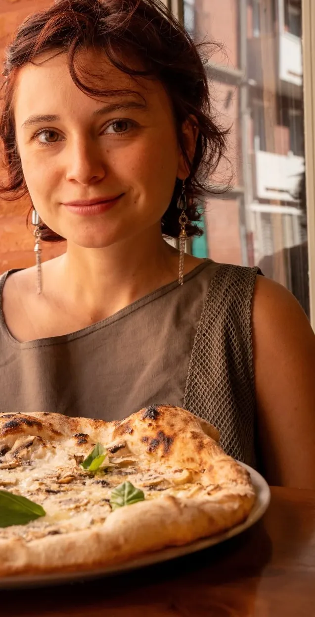 La cliente sourit derrière sa pizza tout juste servie